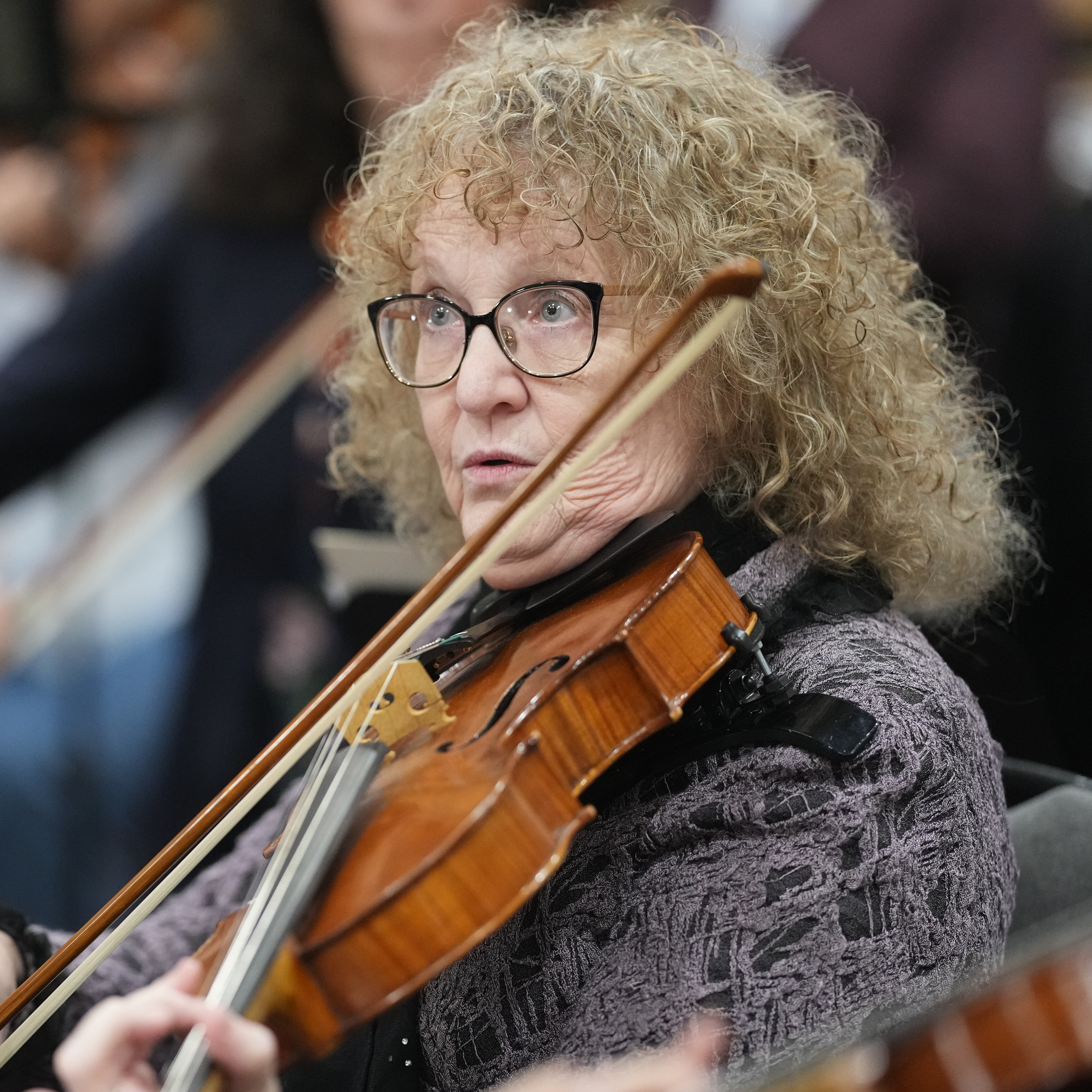 A violinist with curly hair plays in an orchestra, focused and attentive.