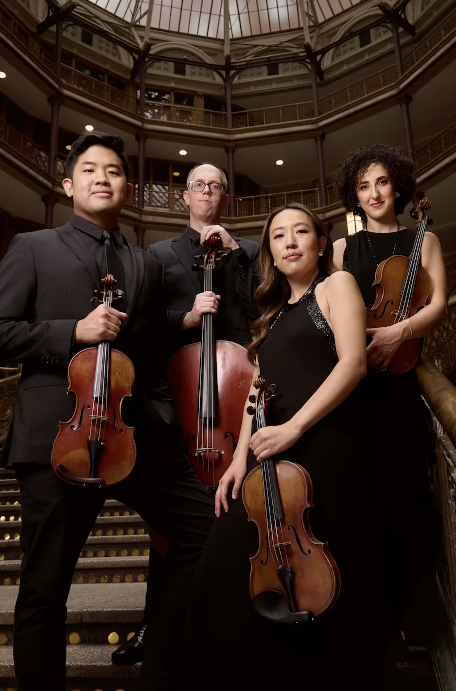 String quartet in formal attire poses on ornate staircase, each holding their instrument.
