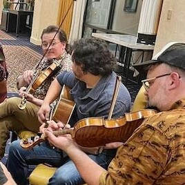Group of musicians playing violins and guitar in a casual setting.