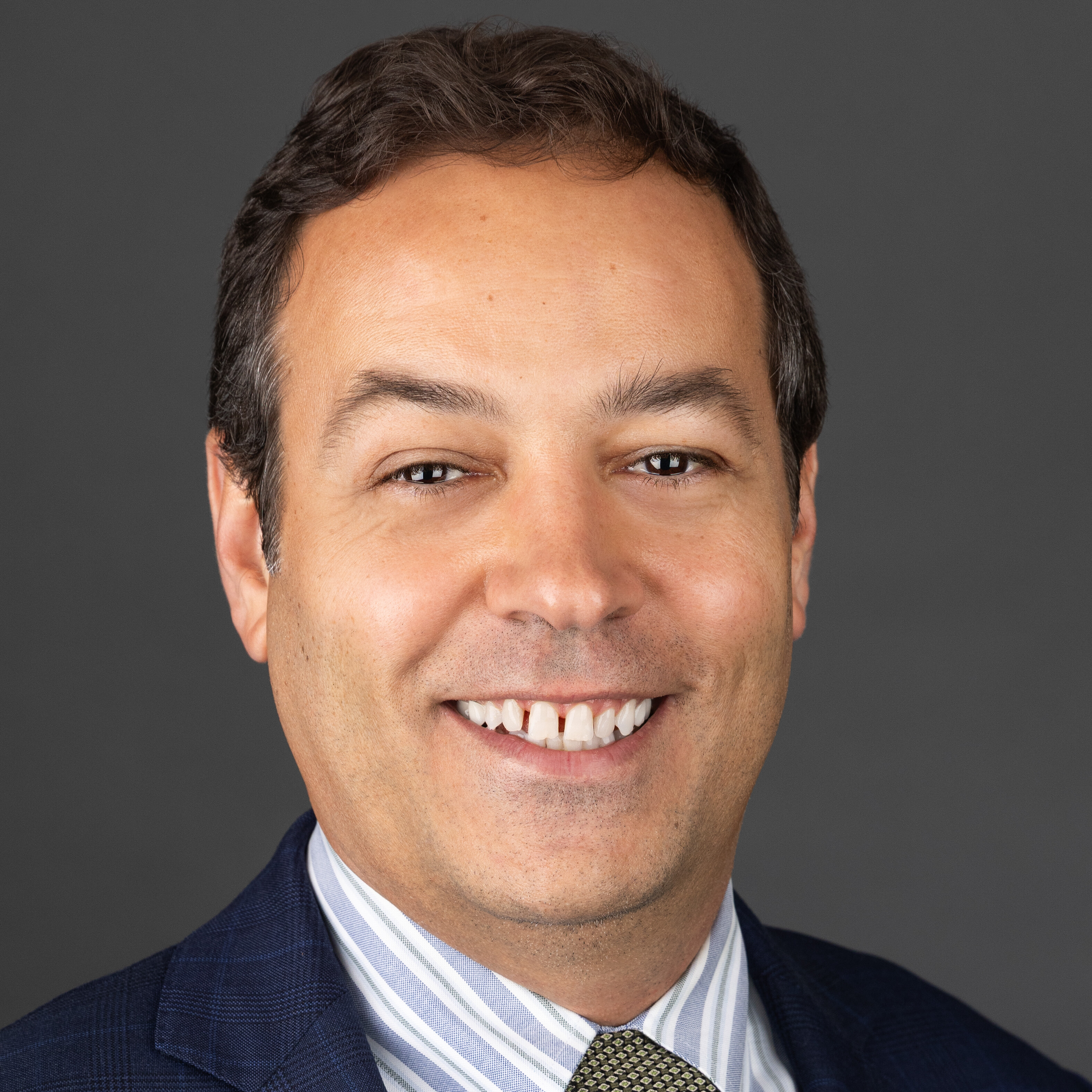 Smiling man wearing a suit and striped shirt against a gray background.