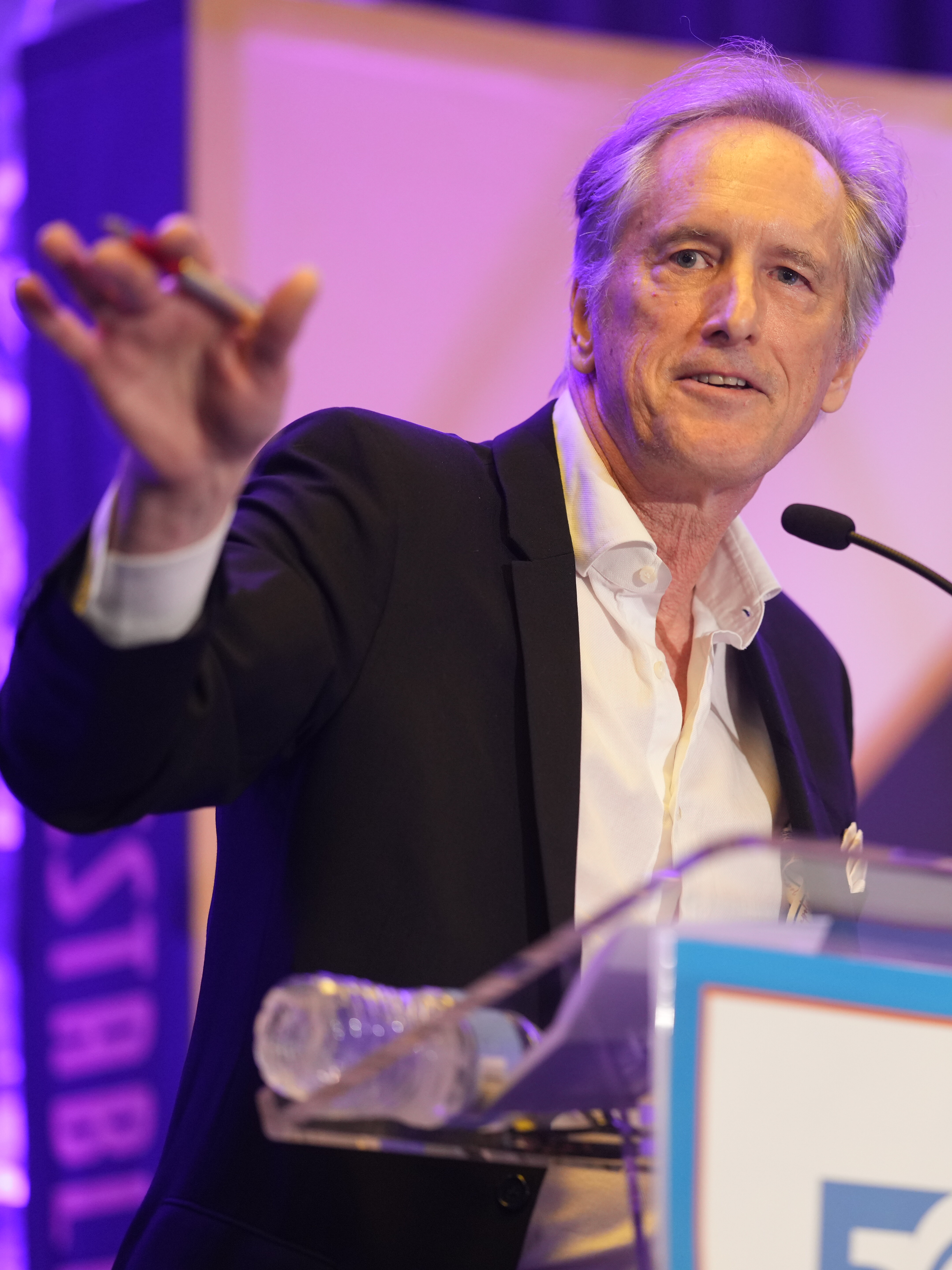 A speaker gestures while addressing an audience at a conference event.