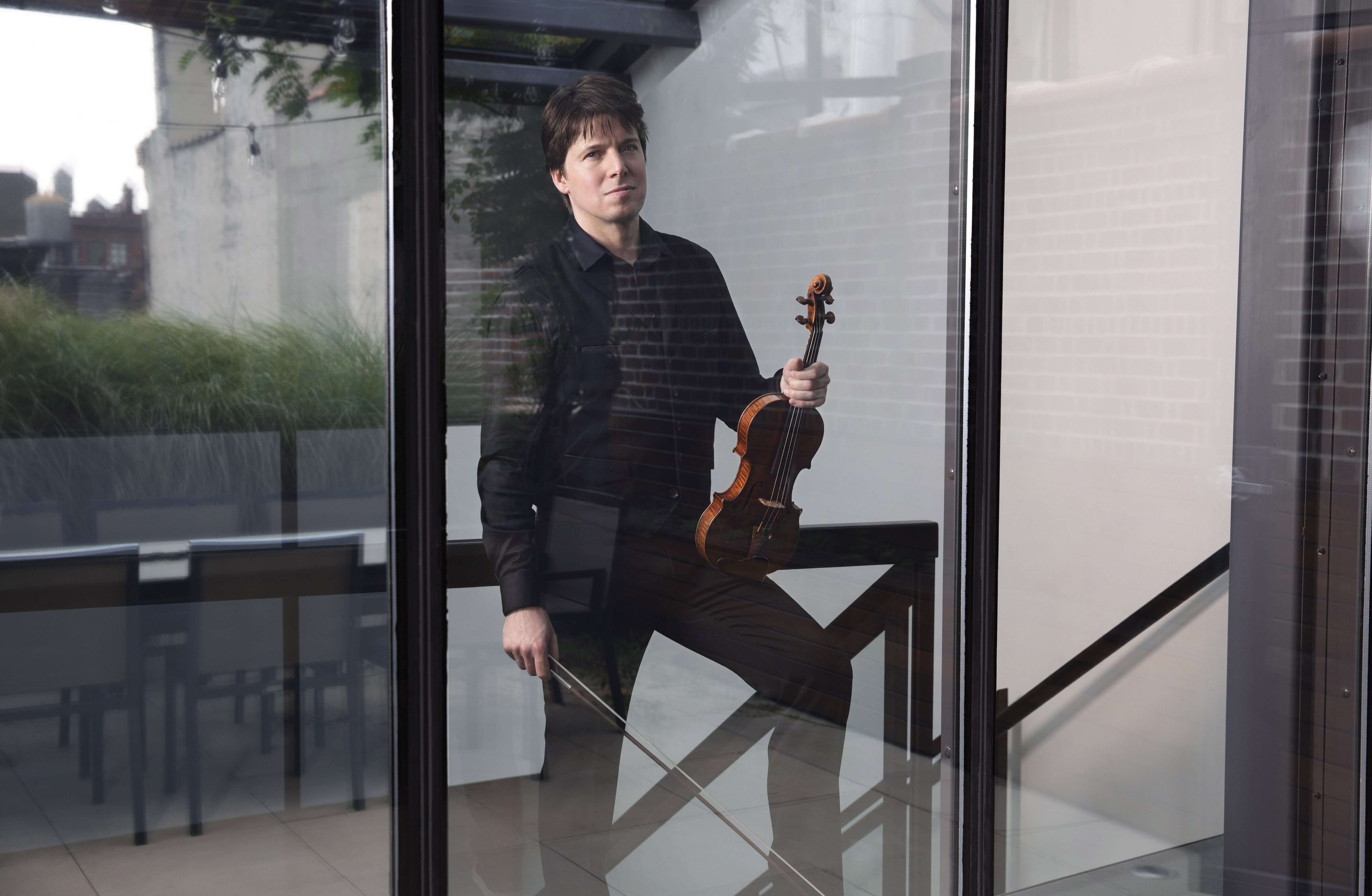 Joshua Bell standing outside a glass window with violin