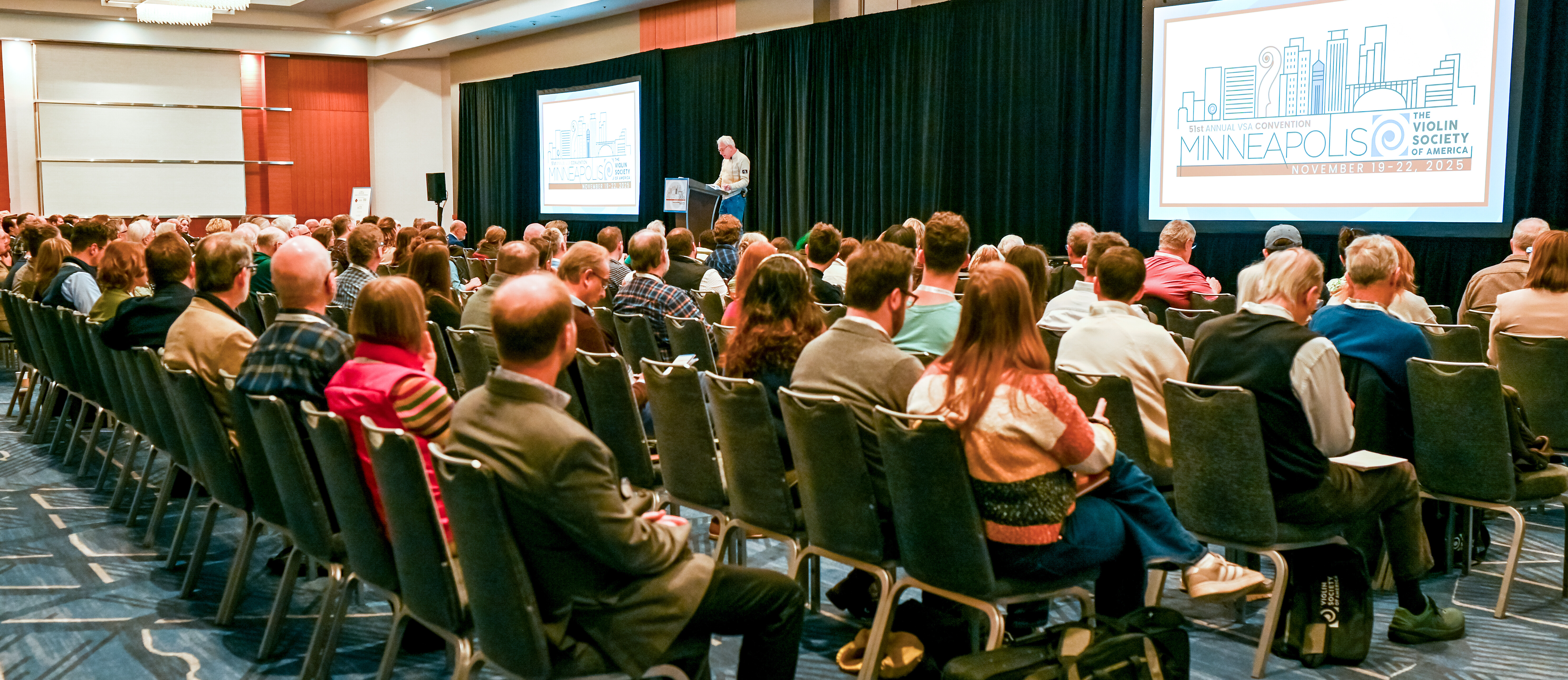 Audience attending the Violin Society of America convention, featuring a speaker onstage.